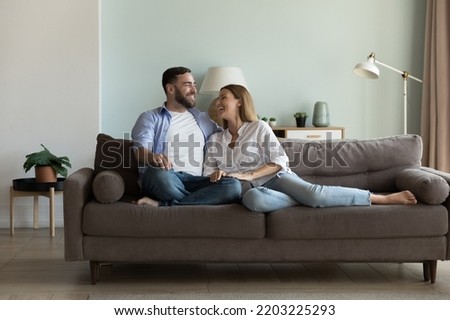 Happy joyful married couple resting on comfortable couch together, enjoying being at new cozy home, talking, laughing, having fun. Relationship, love, real estate for family concept Royalty-Free Stock Photo #2203225293