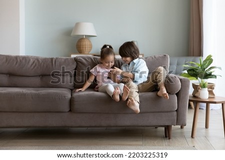Two curious smart gen Z brother and sister kids playing video games on smartphone, using online app, calling to parents, watching Internet content, resting on sofa at home alone Royalty-Free Stock Photo #2203225319