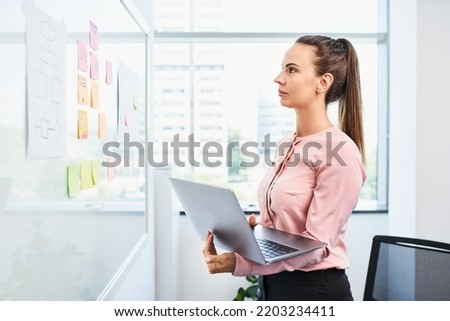 Female entrepreneur brainstorming standing at a whiteboard with laptop. Businesswoman working at modern office