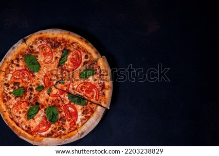 Delicious fragrant pizza-Margherita with mozzarella, tomatoes and basil on tomato sauce on black background. Copy space.