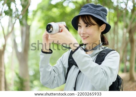 attractive asian woman holding digital camera trekking in forest