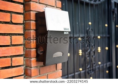 metal post box on brick wall and white address plaque, selective focus
