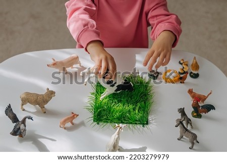 A little girl playing with farm animals on the table in nursery. Educational game. Learning through play. Montessori material concept for toddlers. 