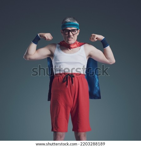 Ridiculous skynny superhero with glasses and small cape showing off muscles, he has a funny aggressive expression Royalty-Free Stock Photo #2203288189