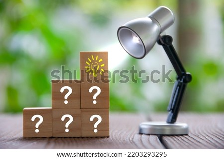 Question marks and light bulb on wooden blocks with table lamp shining. Ideas concepts.