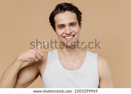Attractive satisfied young man he 20s perfect skin wear undershirt point index fingers on face smile isolated on plain pastel beige background studio. Skin care healthcare cosmetic procedures concept Royalty-Free Stock Photo #2203299969