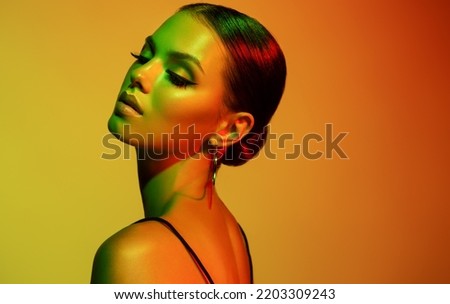 Fashion model woman in colorful bright lights with trendy makeup . Beautiful girl with earrings  jewelry  Beauty and accessories. Neon  and orange with green color