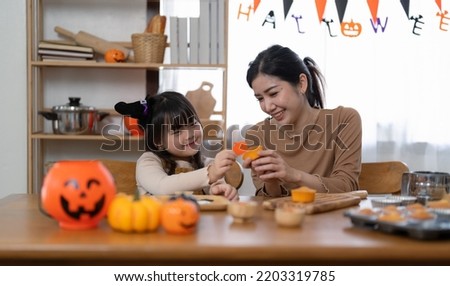 Happy smiling family mother and daughter making Halloween home decorations together while sitting at wooden table.