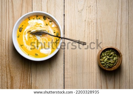Yellow Pumpkin Soup with cream, pumpkin seed, and parsley on wooden background. Copy space. Top view.