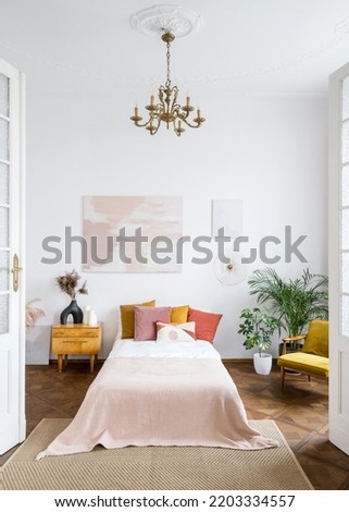 The style of the 60s concept. Bright vintage bedroom in apartment with retro interior design. Houseplants in room with authentic chandelier on a high ceiling over tidy bed, side table, armchair Royalty-Free Stock Photo #2203334557