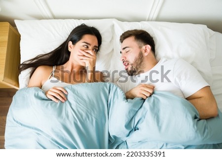 Upset latin woman covering her nose because of the bad breath of her sleeping partner in bed Royalty-Free Stock Photo #2203335391