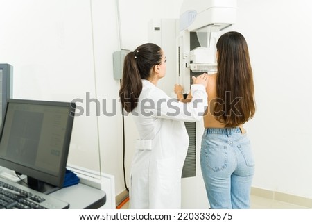 Female radiologist and young woman seen from behind doing a medical mammogram to check for breast cancer