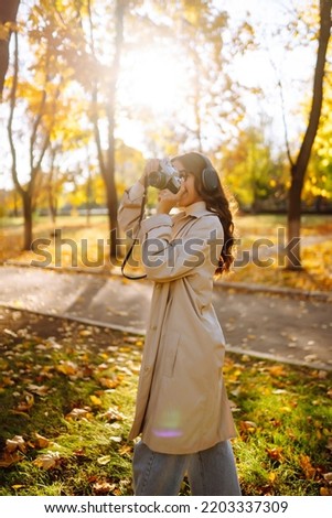 Portrait of  beautiful woman taking pictures in the autumn forest. Smiling woman enjoying autumn weather. Rest, relaxation, lifestyle concept.