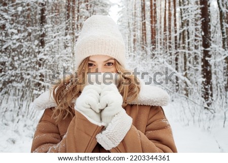 Winter walk, a young beautiful blonde in winter clothes walking in a snowy forest, a beautiful frosty day. A young woman warms her nose wrapped in a white scarf Royalty-Free Stock Photo #2203344361