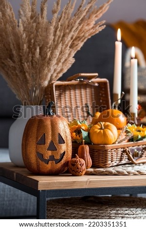 A wicker basket with pumpkins, Jack's Pumpkin and candles in the interior of the living room on a wooden table. The concept of home comfort. Autumn decor for Halloween.