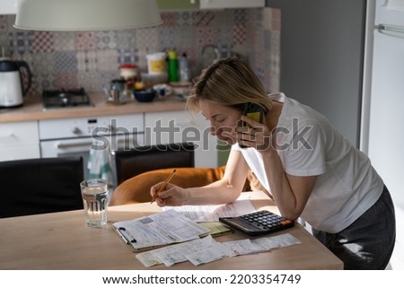 Busy mature woman looks and reads unpaid bills. Middle ager female talks on smartphone with hotline trying to solve problems with obligations and want to pay bills via Internet. Utility debt concept Royalty-Free Stock Photo #2203354749