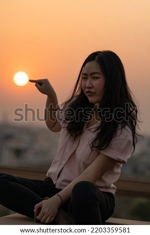 Asian Chinese Thai woman plays with the sun shape on rooftop in twilight time.