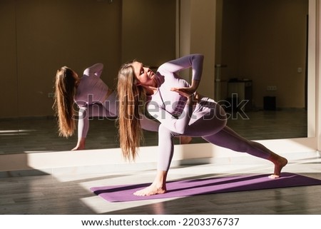 Slim pacified positive caucasian fitness model in purple suit doing virabhadrasana standing on blue rugs of a bright living room. Concept of quarantine home workouts. Advertising space