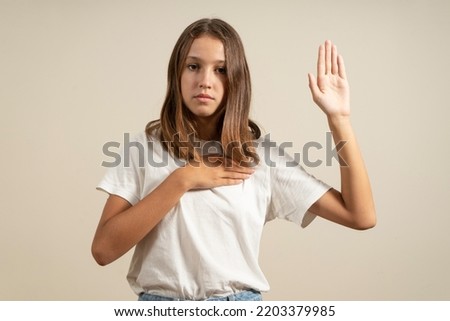 Young brunette hispanic teenager standing together over isolated beige background swearing with hand on chest and open palm, making a loyalty promise oath. Royalty-Free Stock Photo #2203379985