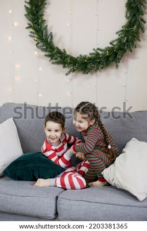 Preschool boy and girl in Christmas pyjamas sitting on a grey sofa