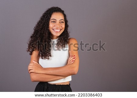 Young Brazilian black woman, with arms crossed, smiling.