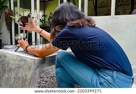 a teenage woman taking a video with a mobile phone in a café