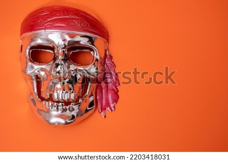 a silver skull with a red headband on a red background. Halloween, piracy. Jolly Roger. The sign of the pirates. Crimes of robbery, Sea robbers. Banner. Space for text. Copy space