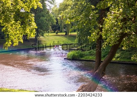 A landscape with a canal, green trees and a rainbow over it
