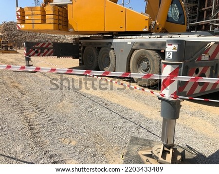 Outriggers of heavy all-terrain mobile crane at construction site. Crane work execution area fenced with a signal tape. Exclusion dropped zone Royalty-Free Stock Photo #2203433489