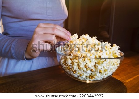 The girl reaches for the popcorn in a glass cup in the kitchen. Getting ready to watch a movie. High quality photo