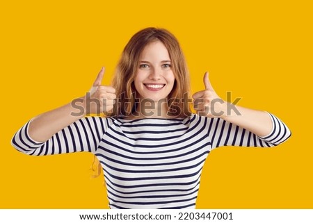 Happy woman giving thumbs up. Portrait of beautiful young blonde girl isolated on yellow background looking at camera, smiling and showing like gestures with both hands Royalty-Free Stock Photo #2203447001