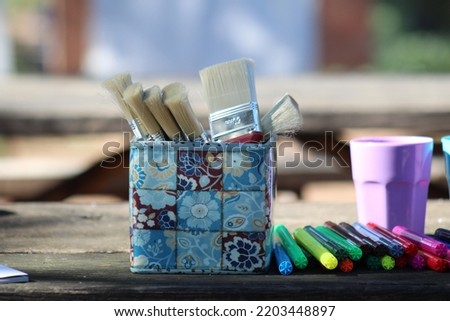 Art supplies (paintbrushes and markers) placed on a wooden table in open air on a sunny day. 
