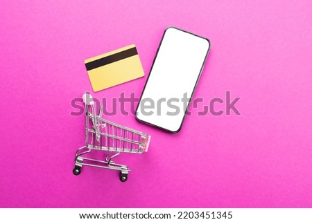 Composition of shopping cart, credit card and smartphone with copy space on pink background. Retail, shopping and black friday concept.