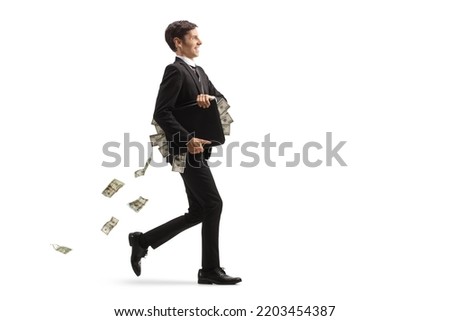 Full length profile shot of a young businessman walking with a briefcase and money falling behind isolated on white background