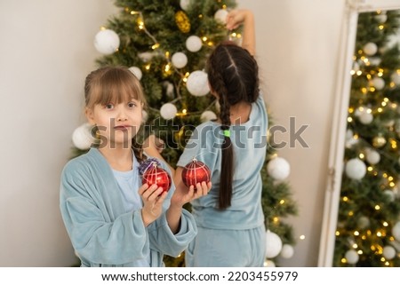 christmas, x-mas, winter, happiness concept - two adorable girls playing near the Christmas tree