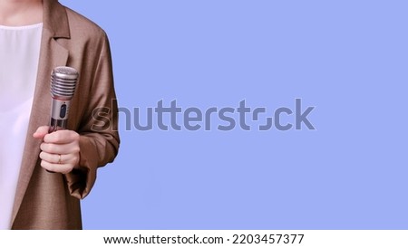 Woman teacher holding microphone in hand on studio blue background, banner copy space