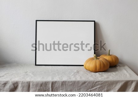 Moody autumn still life. Landscape black picture frame mockup. Orange pumpkins on linen table cloth. White wall background. Minimal rustic interior, neutral color. Halloween, Thanksgiving concept.
