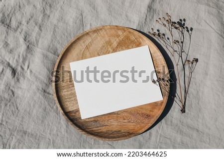 Blank greeting card card mockup on wooden plate, tray. Dry grass, plant in sunlight. Beige linen background, shadow overlay. Modern template for branding identity. Autumn, winter design. Flat lay, top