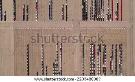 Parked new cars at the car automotive plant manufacturer lot. Electric hybrid cars vehicle factory. Aerial. Almost empty stock. Broken supply chain and chip shortage lead to car shortage availability