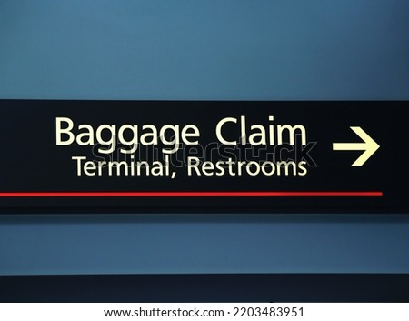 Airport Sign Pointing The Way To Baggage Claim Terminal And Restrooms With Blue Wall Background United States