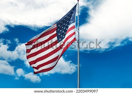 Large American flag waving in the wind against a cloudy blue sky. Low angle view of stars and stripes on american flag against blue sky