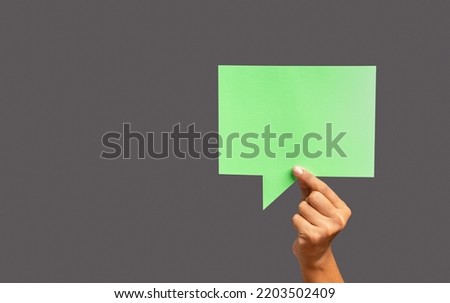 Conversation bubble concept. Close-up of hand holding a green speech bubble against a gray background in the studio. Close-up photo. Space for text