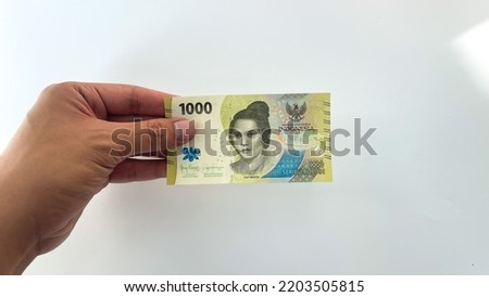 male hand holding new rupiah banknote in 2022. new 1,000 or one thousand rupiah denomination isolated on white background
