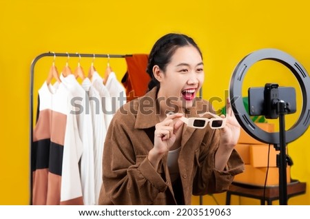 Live streaming concept, young asian blogger woman  showing sunglasses in front of smartphone camera while recording vlog video live chat and selling on her online shop at home.