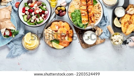 Greek food background. Meze, gyros, souvlaki, fish, pita, greek salad, tzatziki, assortment of feta, olives and meatballs. Traditional different greek dishes set. on a grey background. Top view.