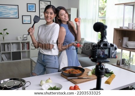 Young Asian lesbian couple blogger influencer vlogger shooting video in kitchen. LGBT couple live- streaming cooking class from home.