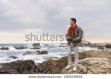 A tourist with a backpack on his back stands against the backdrop of a beautiful seascape