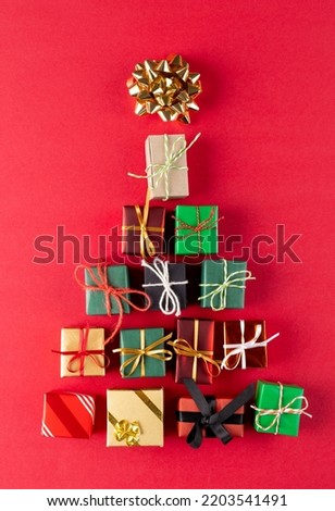 Image of christmas gifts forming christmas tree and copy space on red background. Christmas, tradition and celebration concept.
