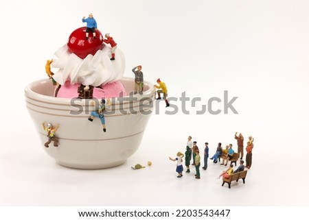 Miniature climbers ascend a bowl of ice cream with an audience. Royalty-Free Stock Photo #2203543447