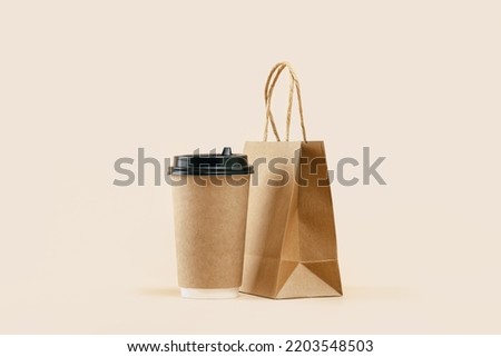 Takeaway paper coffee cup with lunch bag on beige. Snack delivery service. Coffee to go. Grab and go or carry out beverage. Disposable mockup packaging. Place for text. Minimal Royalty-Free Stock Photo #2203548503